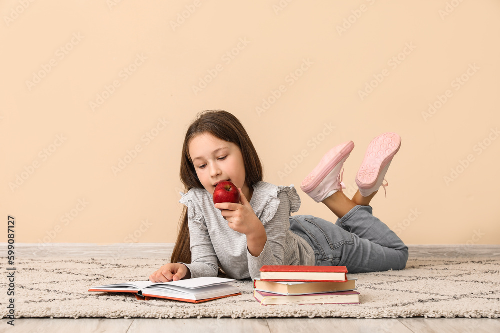 Little girl with apple reading book near beige wall. Children's Day celebration