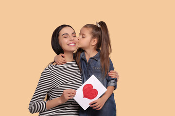 Wall Mural - Happy woman with her cute daughter and handmade greeting card on beige background, space for text. Mother's day celebration