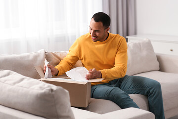 Wall Mural - Happy young man opening parcel at home. Internet shopping