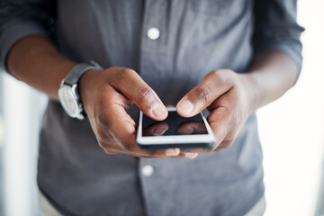 Poster - Maintaining a social presence is essential in business. an unrecognizable businessman standing alone in his office and using his cellphone.
