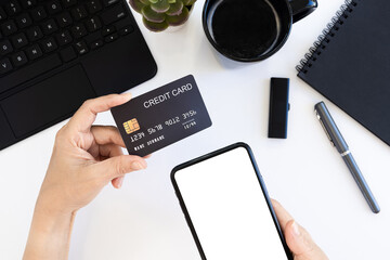 Wall Mural - Online payment Concept. Woman using credit card with mobile phone and coffee cup on white office desk.