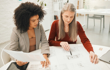 Wall Mural - Mature businesswoman working with a colleague. Coworkers working on a building project. Team of architects brainstorm and collaborate. Boss working on a blueprint with her staff member.