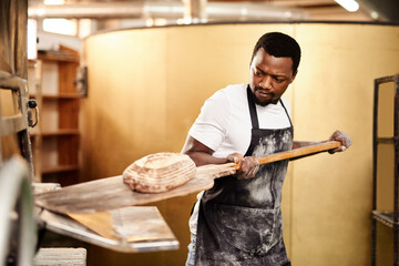 Poster - The home of fresh baking. a male baker removing freshly baked bread from the oven.
