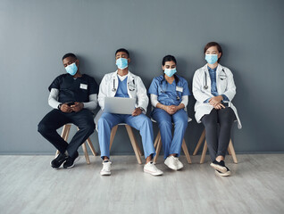 Poster - The real heroes wear scrubs. a group of doctors sitting against a grey background at work.