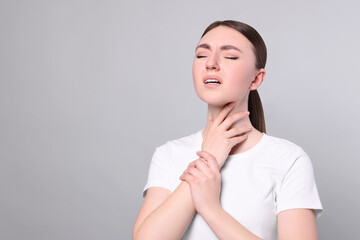 Poster - Young woman with sore throat on light grey background. Space for text