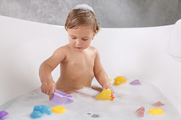 Wall Mural - Cute little girl taking bubble bath with toys indoors