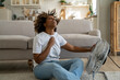 © DimaBerlin - Summer heat. Young African American woman cooling down by ventilator at home, feeling unwell with high temperature during hot weather, sitting on floor in front of electric fan during extreme heatwave