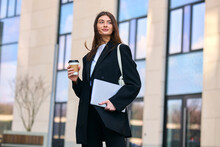 A Successful Businesswoman In A Trendy Blazer Stands Outside A Modern Skyscraper, Enjoying A Coffee While Checking Her Laptop