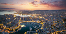 Aerial Panorama Of The Illuminated Piraeus District In Athens, Greece, With Zea Marina And The Ferry Boat Harbour In The Background During Evening Time