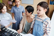 © Seventyfour - Choir of children singing songs in music class while teacher playing piano and singing together with them