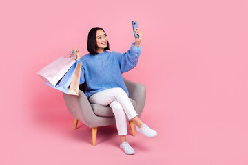 Wall Mural - Full size photo of charming girl sit chair hold smart phone boutique bags make selfie isolated on pink color background