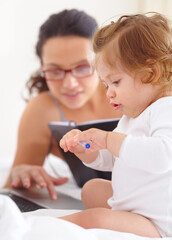 Canvas Print - Keeping her busy while trying to work. A baby girl sitting next to her mother and playing with a ballpoint pen.