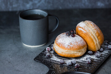 Delicious dessert. A doughnut with berry filling, fresh currant berries, powdered sugar and a cup of black coffee or tea on a dark background. Sweets.