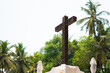 Closeup shot of Crucifix Bom Jesus in front of Palm trees at Basilica of Bom Jesus Church in Goa, India. Cross of jesus christ at old catholic church in Goa. Cross in front of the palm trees.	
