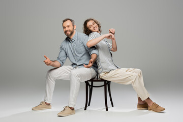 Wall Mural - happy father and carefree teenage son having fun and pushing each other while sitting on same chair on grey.