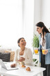 © LIGHTFIELD STUDIOS - cheerful lesbian woman holding glasses with orange juice near multiracial partner working on laptop.