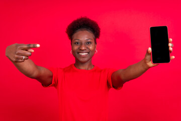 Young african american woman isolated on a red background with mobile pointing gesture, studio shoot