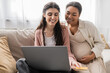 © LIGHTFIELD STUDIOS - cheerful and pregnant multiracial woman looking at laptop while doing online shopping with happy lesbian partner.
