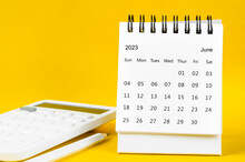 The June 2023 Monthly Desk Calendar For 2023 Year And Calculator With Pen On Yellow Background.