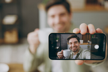 Wall Mural - Clsoe up young fun man wears casual clothes doing selfie shot on mobile cell phone post photo on social network drink tea sits alone at table in coffee shop cafe restaurant indoors rest relax inside.