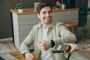 Wall Mural - Young man wear casual clothes sit alone at table in coffee shop cafe restaurant indoors work or study on laptop pc computer hold bank terminal to process acquire smart watch payment Freelance concept