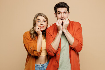 Wall Mural - Young shocked scared fearful couple two friends family man woman wear casual clothes looking camera biting nails fingers together isolated on pastel plain light beige color background studio portrait.