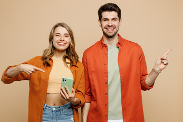 Young fun smiling happy cheerful couple two friends family man woman wear casual clothes hold in hand use mobile cell phone together point aside isolated on pastel plain light beige color background.
