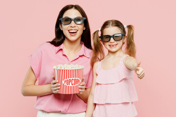 Wall Mural - Young woman wear casual clothes with child kid girl 6-7 year old in 3d glasses watch movie film holding bucket of popcorn in cinema Mother daughter isolated on plain pink background Family day concept
