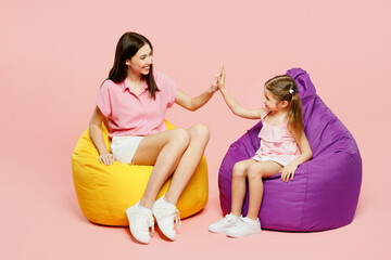 Wall Mural - Full body woman wear casual clothes with child kid girl 6-7 years old. Mother daughter sit in bag chair give high five clapping hand folded isolated on plain pink background Family parent day concept