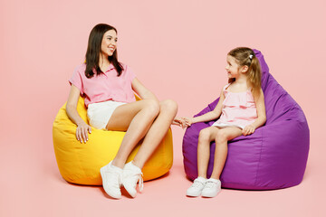Wall Mural - Full body cheerful happy woman wear casual clothes with child kid girl 6-7 years old. Mother daughter sit in bag chair look to each other isolated on plain pink background. Family parent day concept.