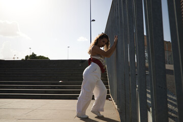 Wall Mural - Young latin woman leaning on steel fence. The woman is a dancer of modern dance. Concept youth and social problems.