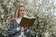 © vladdeep - Portrait of Blonde Woman in Blossom Tree Flowers Holding Book in Hands.