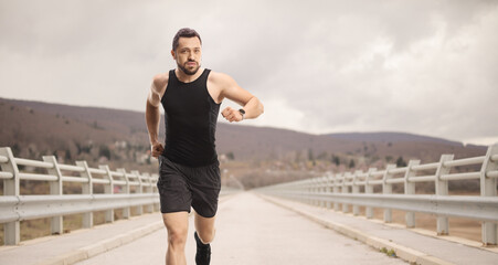 Sticker - Fit young man with a smartwatch running on cloudy day over a bridge