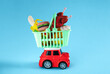 Miniature red car with shopping basket full of food. Colourful delivery concept poster.