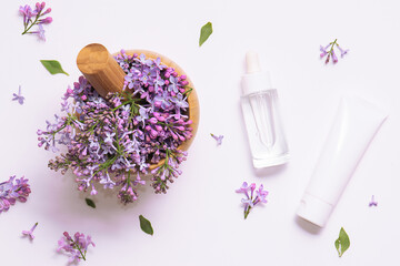 Wooden mortar with fresh lilac flowers and two white cosmetic tubes on white background top view. Natural herbal cosmetic banner.