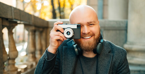 Banner size shot of a smiling bald guy looking through camera taking a picture outdoors.