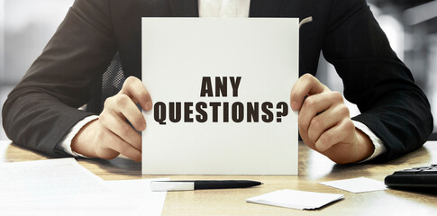 Poster - businessman holding a white card with text any questions on office background