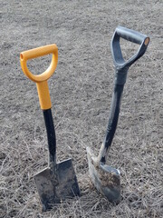 two black dirty steel shovels in the ground and gray dry grass in the field