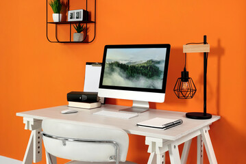 Poster - Modern computer, books, lamp and notebook on wooden desk near orange wall. Home office