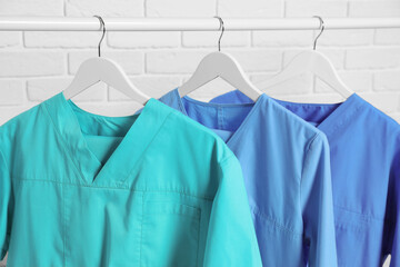 Wall Mural - Medical uniforms hanging on rack near white brick wall, closeup