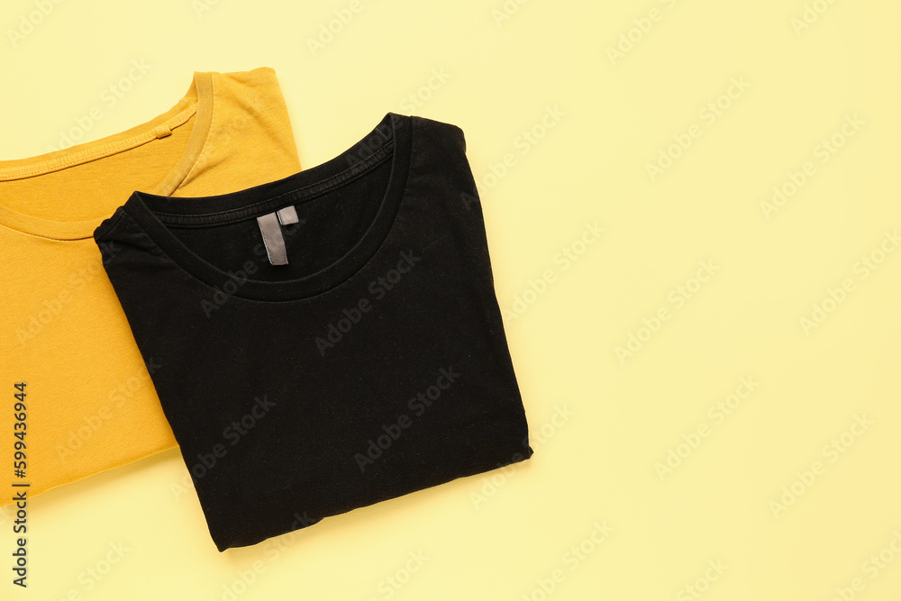 Folded yellow and black t-shirts on color background