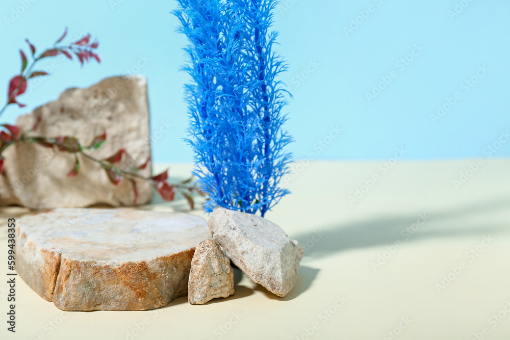 Decorative stone podium and seaweed in sand on blue background
