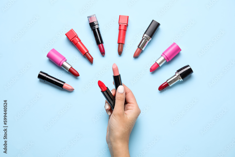 Female hand holding lipsticks on blue background