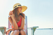 © GR/peopleimages.com - Starting the day off lovely. a cheerful young woman wearing a hat while being seated on a chair next to a lake outside in the sun.