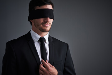 So good, he can do business with his eyes closed. Studio shot of a young businessman wearing a blindfold against a gray background.