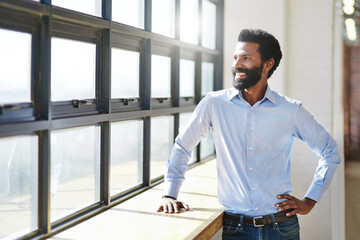 Canvas Print - The sun is shining on his corporate goals. a businessman standing at a window in his office.