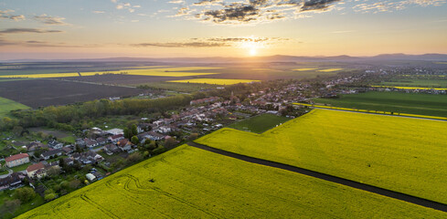 Wall Mural - Aerial sunset with village and rapeseed fields over mountain landscape