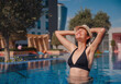 © Seleznov_Molchanova - Portrait of beautiful asian woman in black swimwear and hat relaxing in swimming pool spa. Hot summer day and bright sunny light. Healthy body care in travel