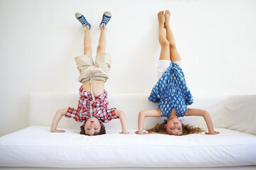 Sticker - Ta da. a playful young brother and sister doing handstands together on the sofa.