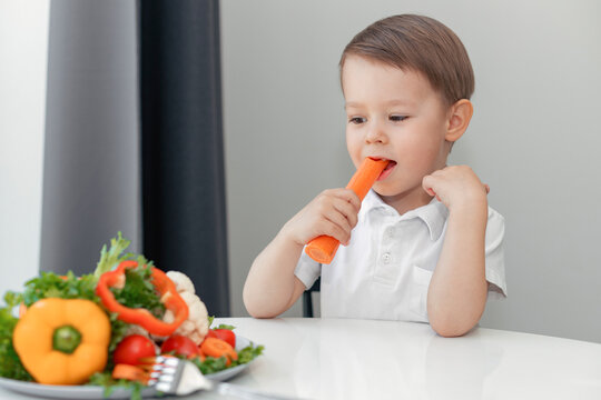 Wall Mural - boy with appetite eats carrots and fresh vegetables at the table at home, the concept of a healthy diet for children